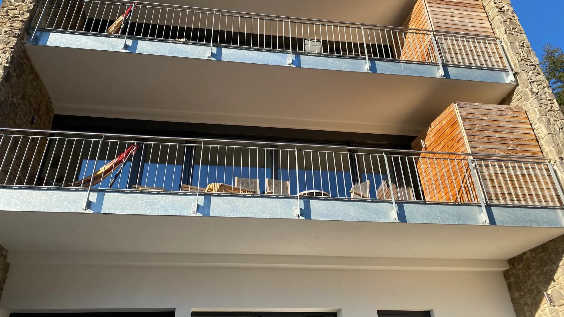 Blick von unten auf die beiden überdachten Balkone mit Hängematte und Liegestühlen