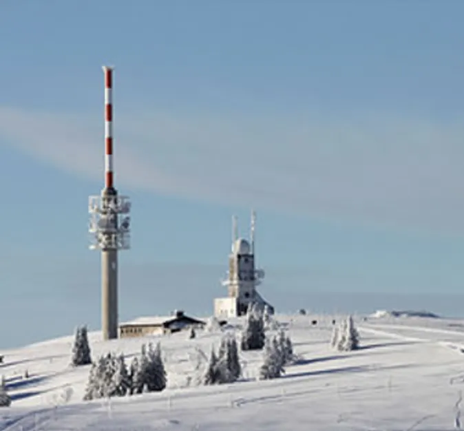Der verschneite Feldberggipfel mit Sendeturm und Wetterstation vor blauem Winterhimmel