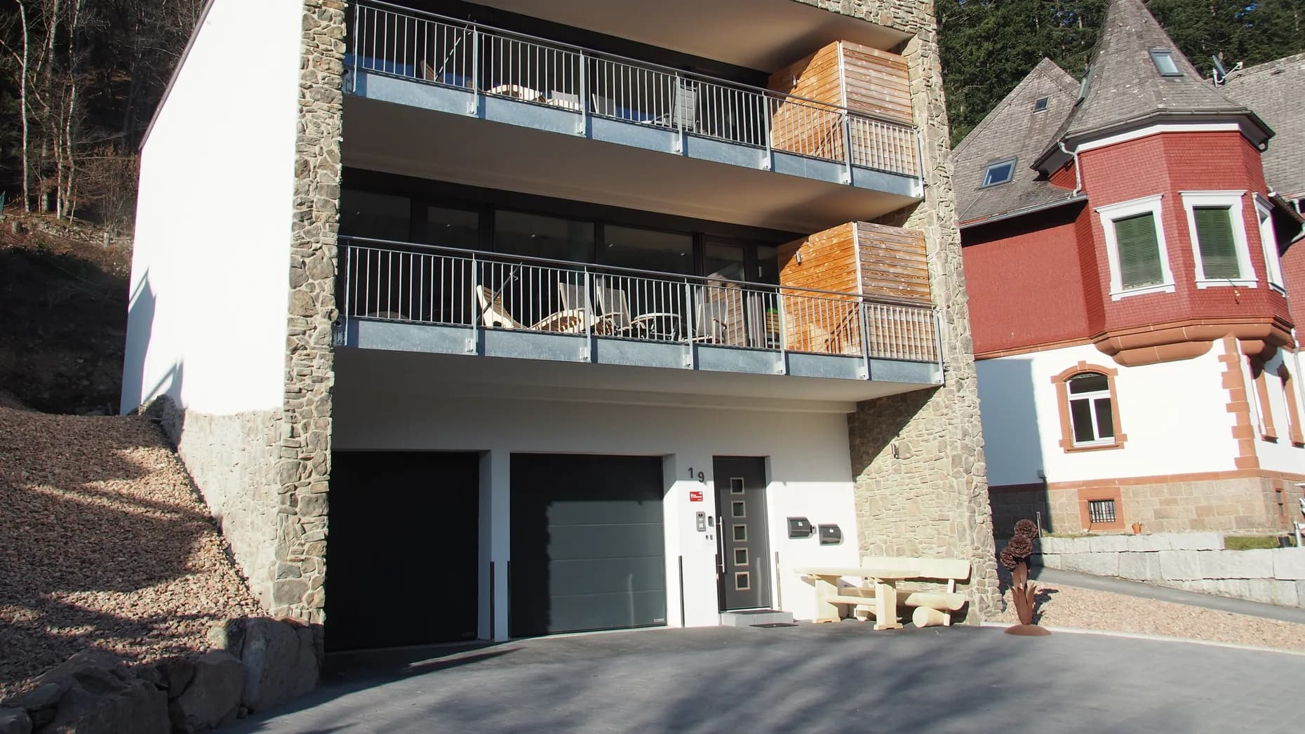 Haus LuFeTo mit Natursteinfassade, dahinter der bewaldete Hang des Hochschwarzwalds